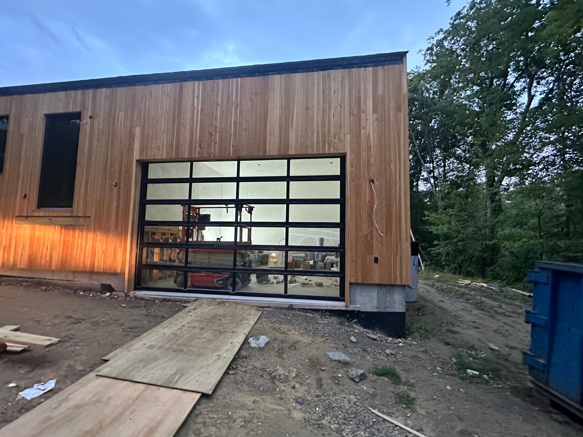 Full-view glass garage door on modern cedar-clad building at dusk